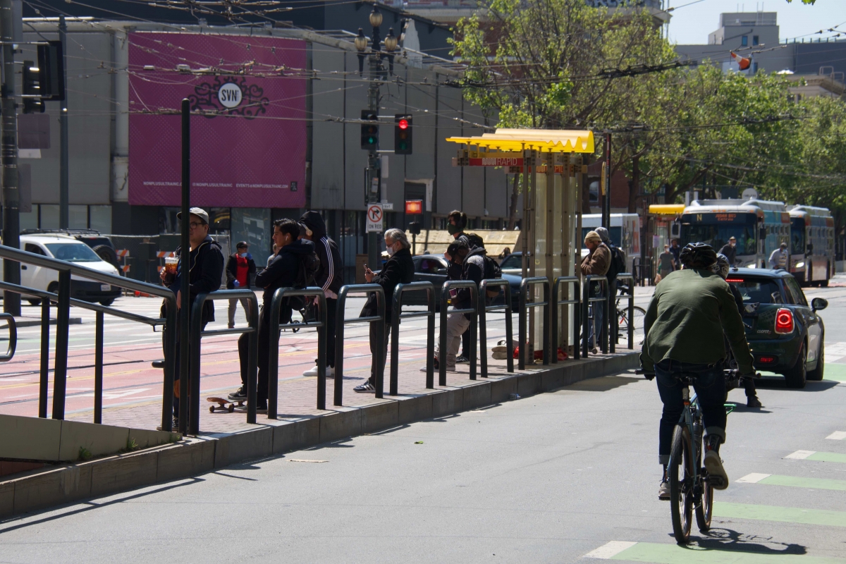 People wait at a stop on Market Street and Van Ness Avenue on April 10. A bus replacing the regular N Judah line and another bus going in the same direction are at another stop across the intersection. 