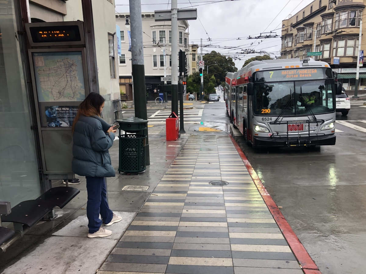 A woman waits on a rainy day for the 7 Haight/Noriega on Haight Street at Divisadero Street on April 6. It was the last day the 7 was running. It was among a smaller group of buses that stopped service on April 7 before wider Muni cuts took effect on April 8.