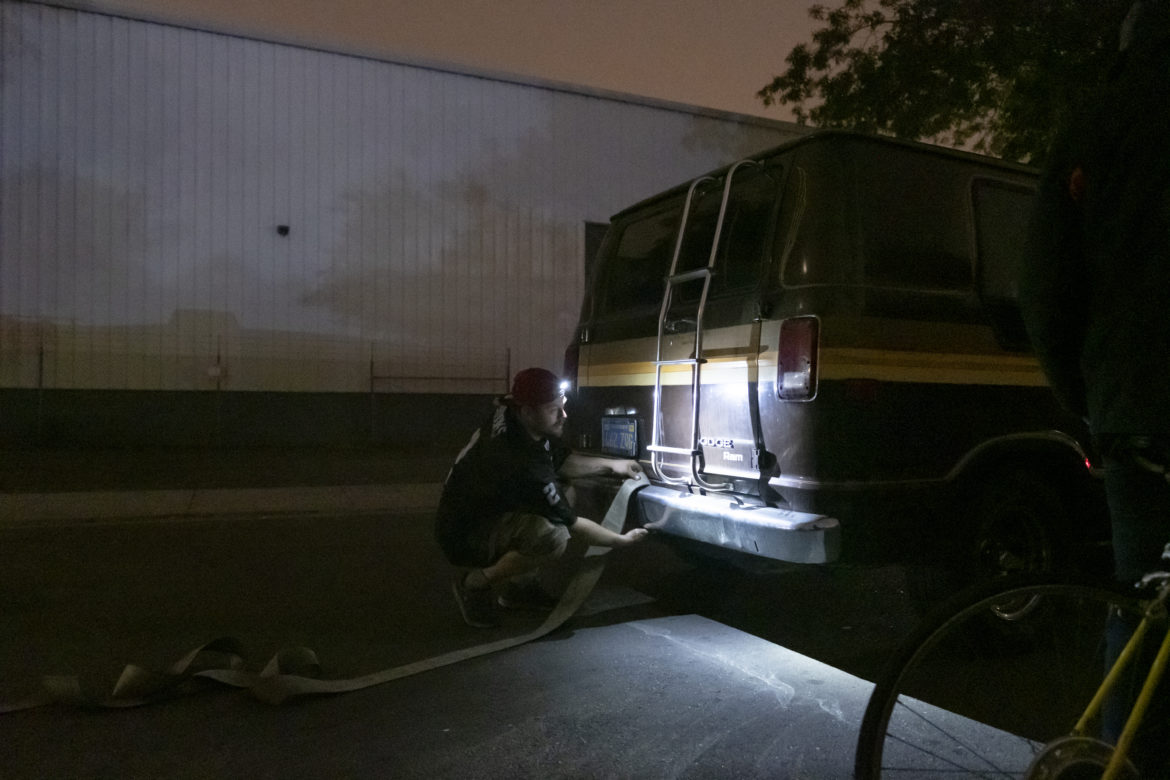 Chris Castle ties a tow strap to the bumper of Amber Whitson’s Dodge van on a Sunday night to help his friend Ryan Maddry, whose vehicle was red-tagged with a 72-hour notice, giving him a warning to move or be towed. But the “Ole Gal” is in disrepair and barely makes it around the corner. As a last resort, vehicle residents band together and use human force, pushing their vehicles by hand or pulling them with ropes. It is challenging to find new parking places and get resituated every three days.