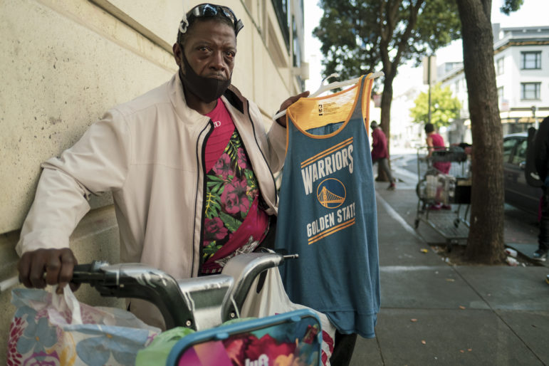 Damon, 47, walks his bicycle down a busy sidewalk in the Tenderloin neighborhood in late June, selling Warrior jerseys for $7. He packs his merchandise on his found Lyft bike and rides it for transportation, avoiding public transit and the coronavirus, he says.