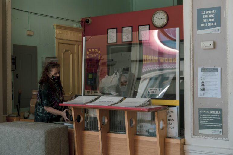 Kristi Banks picks up her mail from the reception desk of Hotel Essex. To prevent the spread of the coronavirus, the hotel installed plexiglass walls and posted safety guidelines. Residents must wear masks when entering the building. The hotel has about 100 rooms on seven floors.