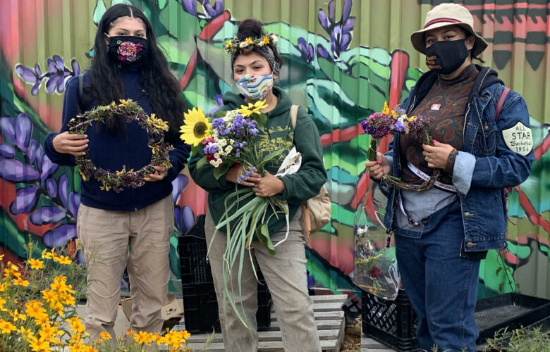 Three people stand and hold flowers and other harvest from Hummingbird Farm.