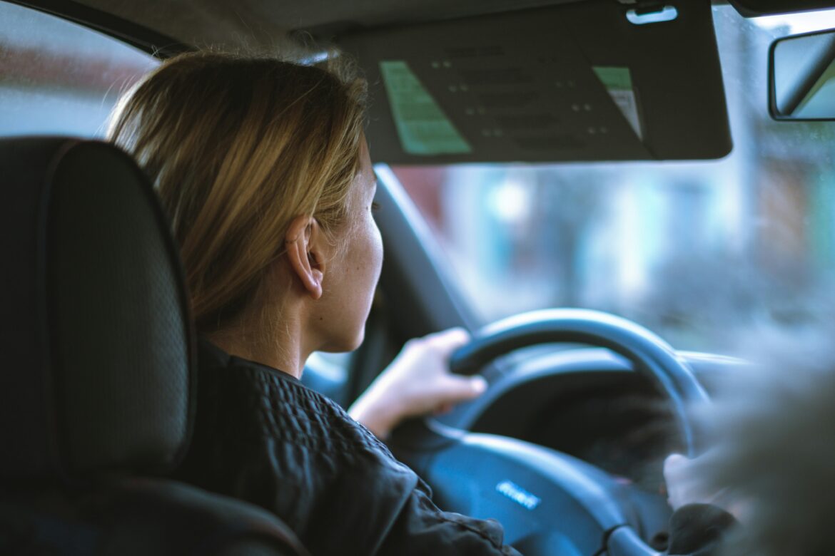 A woman sitting in a car, behind the steering wheel.