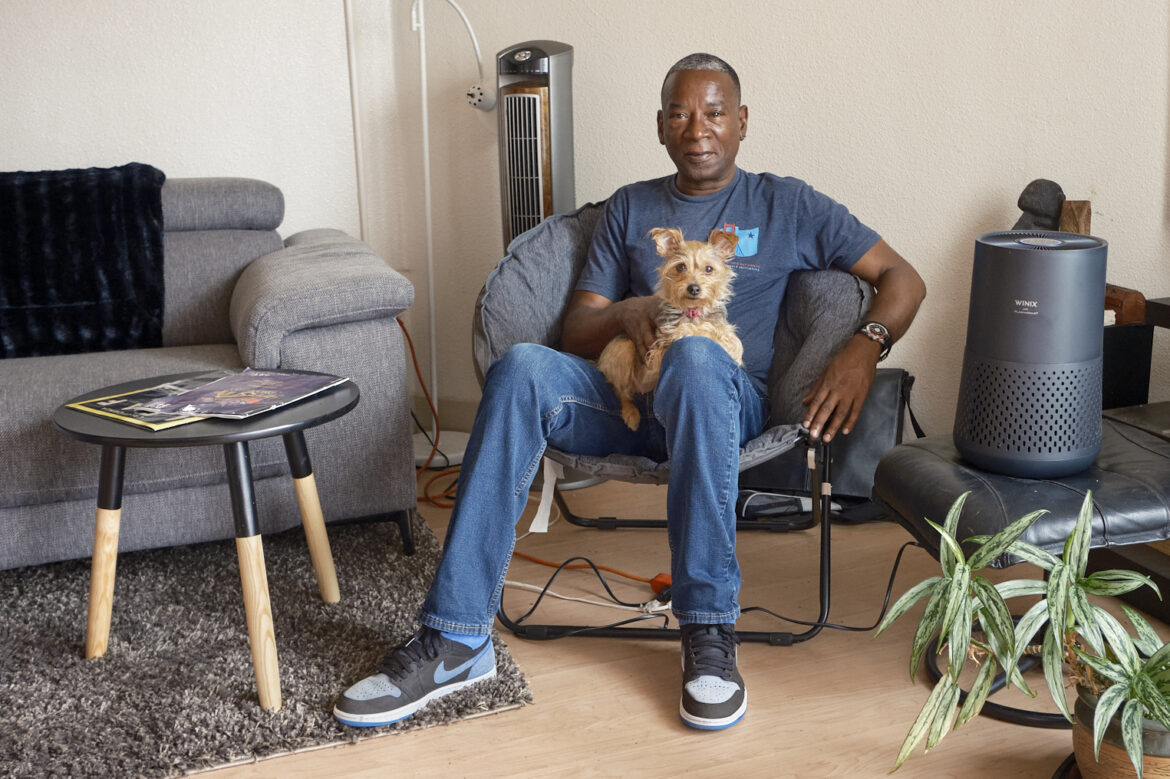 John Britt sits in his apartment with his dog on his lap, and his air purifier to his left.