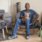 John Britt sits in his apartment with his dog on his lap, and his air purifier to his left.