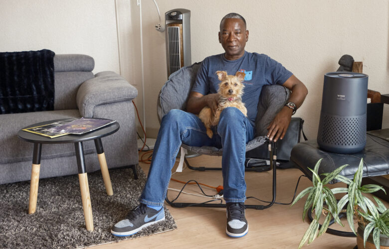 John Britt sits in his apartment with his dog on his lap, and his air purifier to his left.