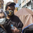 Two homeless people, with face masks, stand in front of their tent in San Francisco's Tenderloin neighborhood.