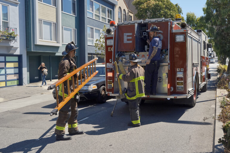 Firefighters handle a ladder and other gear in the field.