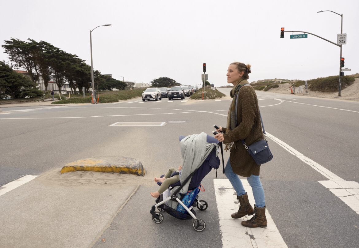 A woman crosses the street with a stroller and child at the intersection of Lincoln Way and the Great Highway.